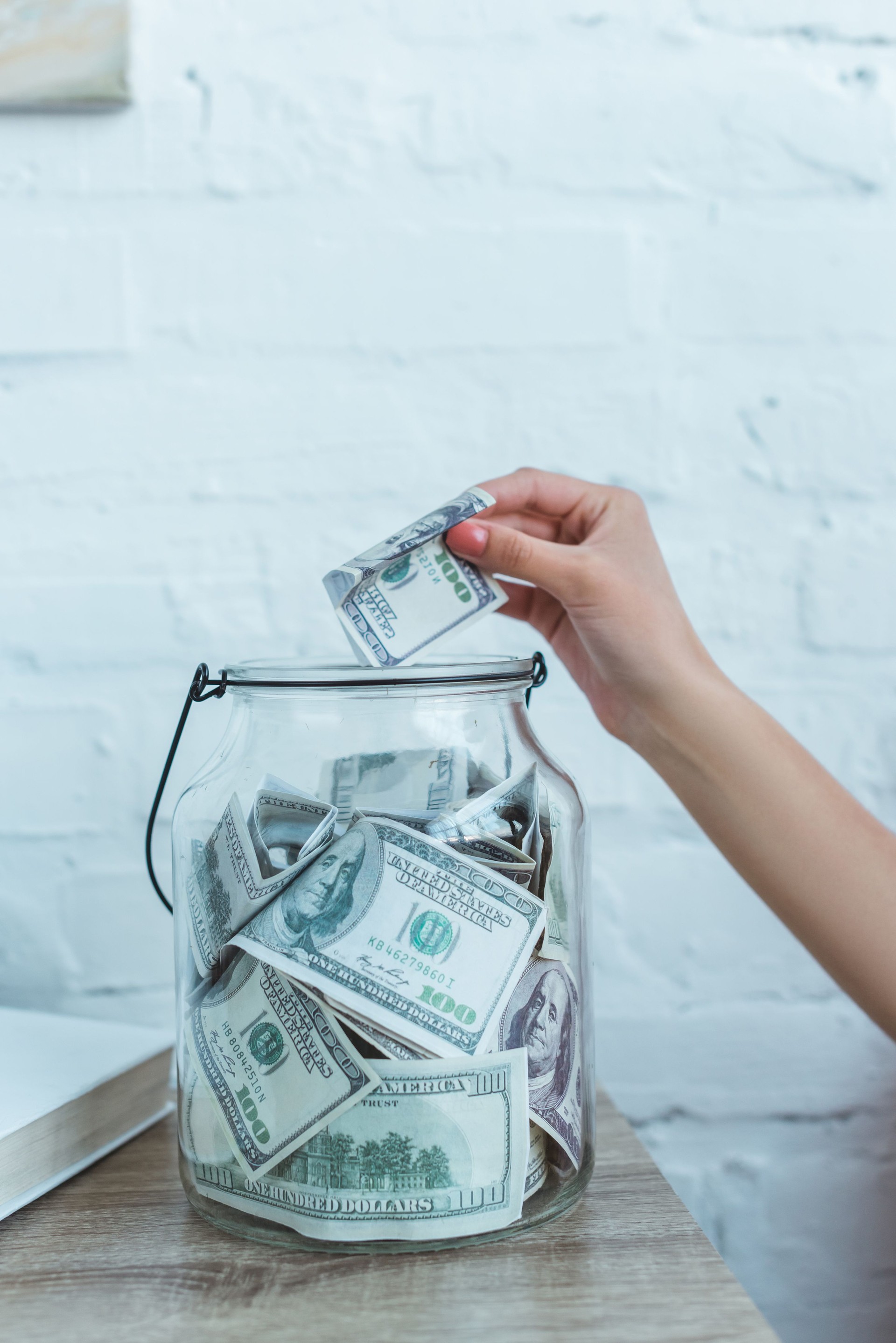 cropped view of female hand putting dollar banknote into glass jar