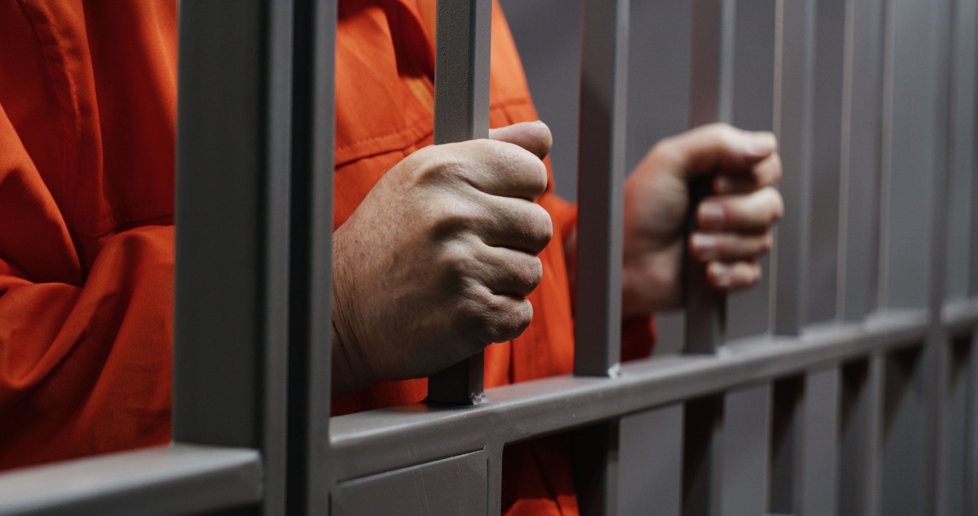 Hands close up of elderly prisoner holding metal bars