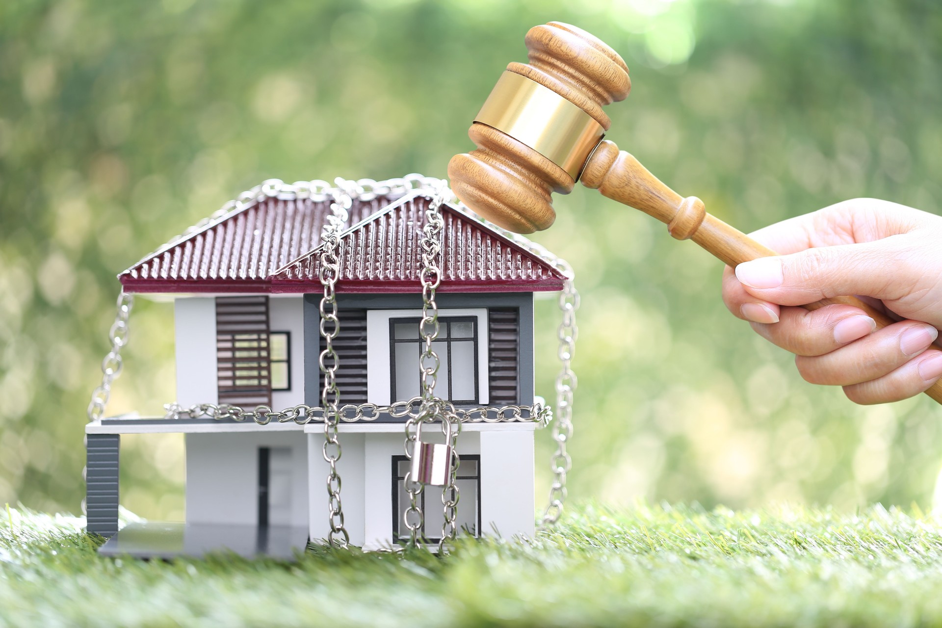 Property auction, Woman hand holding gavel wooden and locked house with padlock and chain on natural green background, lawyer of home real estate and ownership property concept.bankruptcy