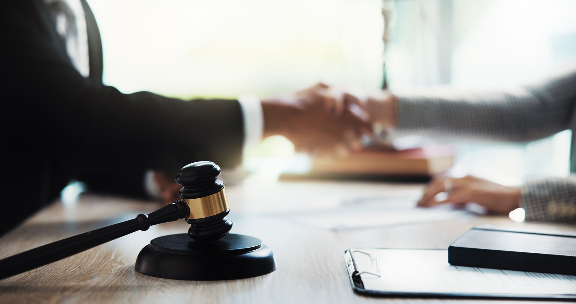 Judge, handshake and lawyer in office with gavel on table for legal agreement. Attorney, business people and shaking hands for success, justice and support with lawsuit settlement or negotiation